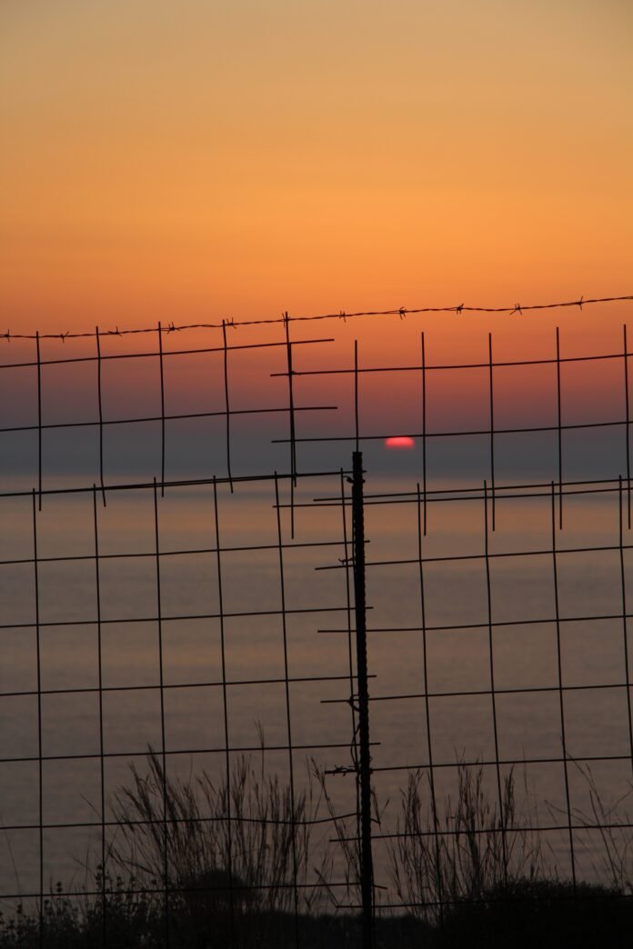 Beautiful shot of the sunset over the ocean behind the metal fence in Crete