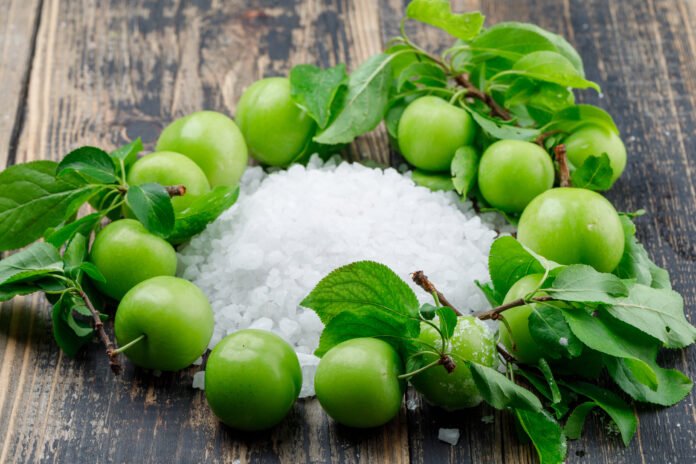 Green plums with salt crystals, leaves high angle view on a wooden background