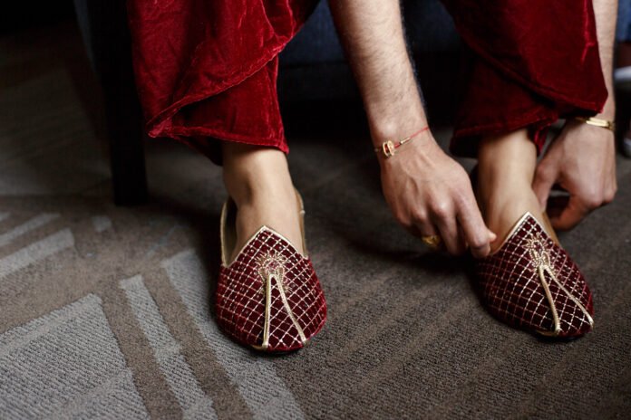 Groom in red velvet trousers puts on golden wedding shoes