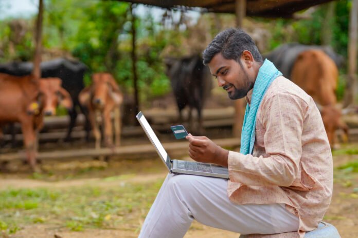 Young indian farmer using laptop and card at his farm